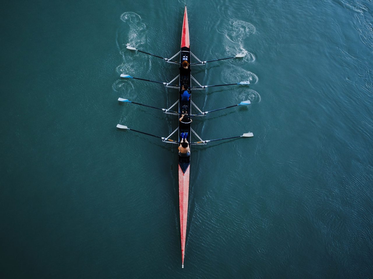 Kayak from above with 4 rowing people. Blue and aqua water background. Sport and moving concept. Red kayak and 8 paddles.